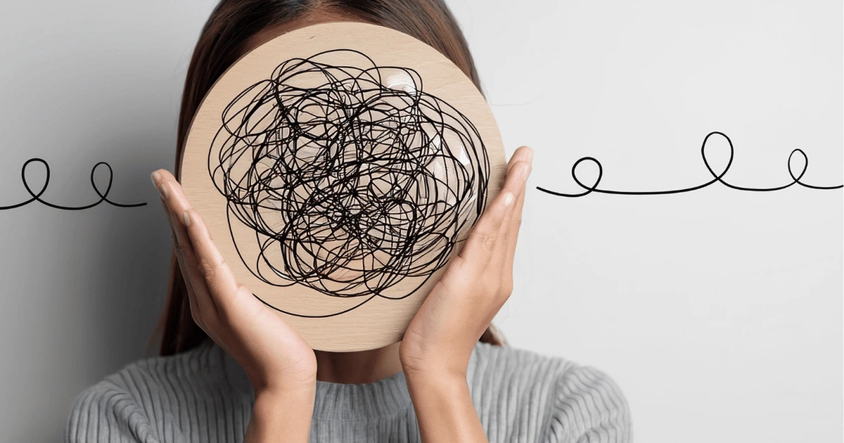 Personne tenant un masque avec des lignes emmêlées devant son visage, représentant la surcharge mentale et le trop-plein intérieur.