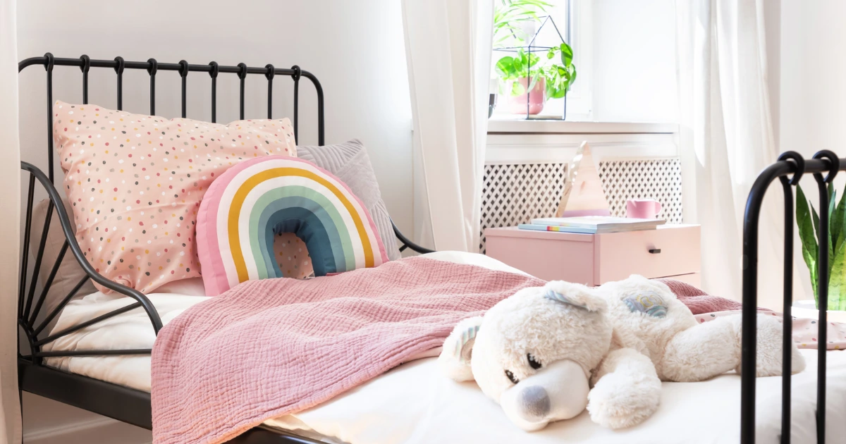 Chambre d’enfant lumineuse avec lit, coussins colorés et peluche illustrant l’article "Les 5 espaces indispensables pour une chambre d’enfant facile à organiser.